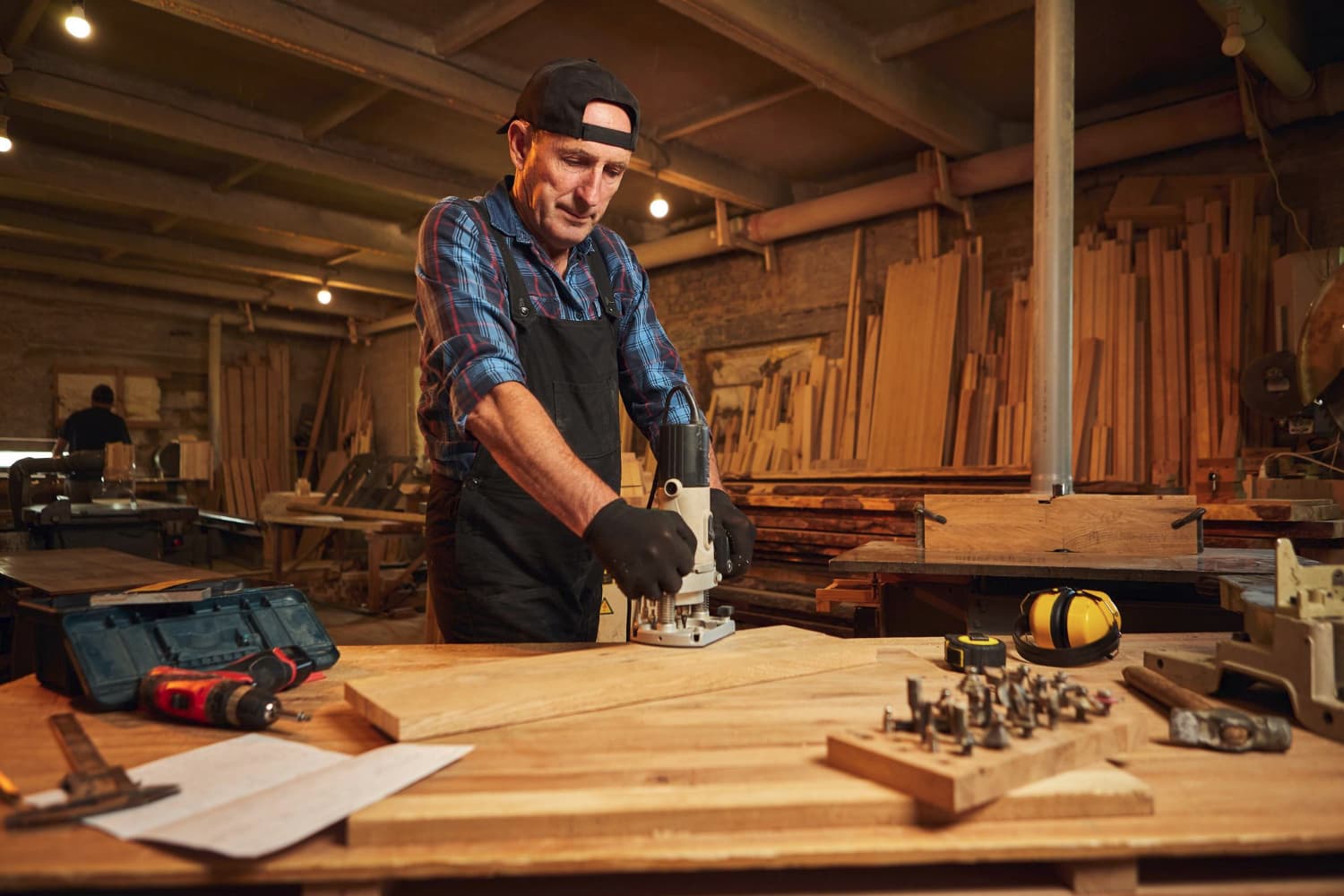 A man is engaged in woodworking at a table, concentrating on his craft amidst scattered tools and wood shavings.